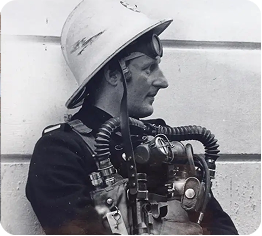 Historic firefighter wearing early breathing apparatus and helmet.
