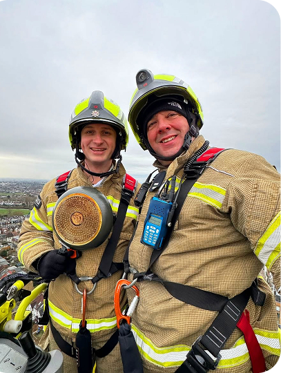 Two firefighters in safety gear posing at height.
