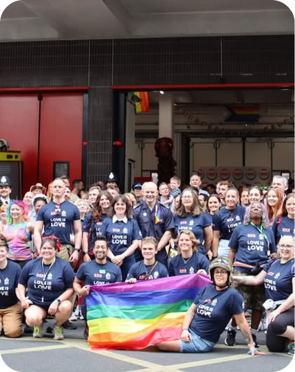 Group holding rainbow flag outside fire station Pride event.